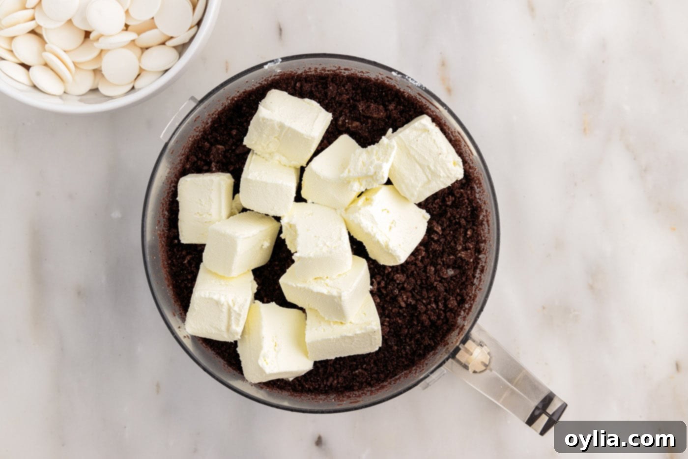 Adding cream cheese cubes to the food processor with crushed Oreos.
