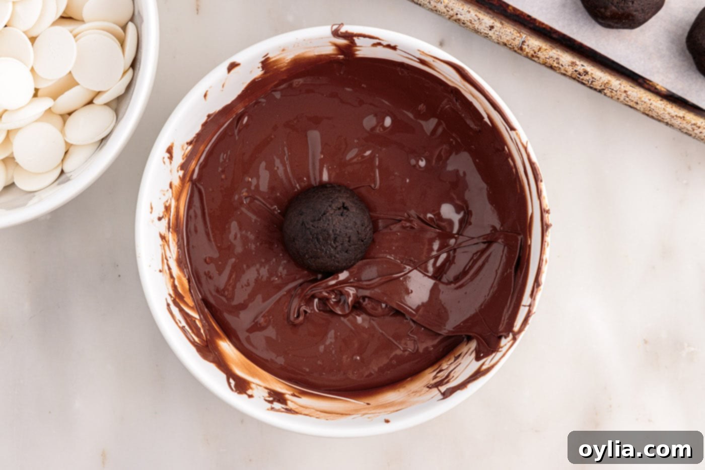 Oreo balls being dipped into a bowl of melted chocolate.