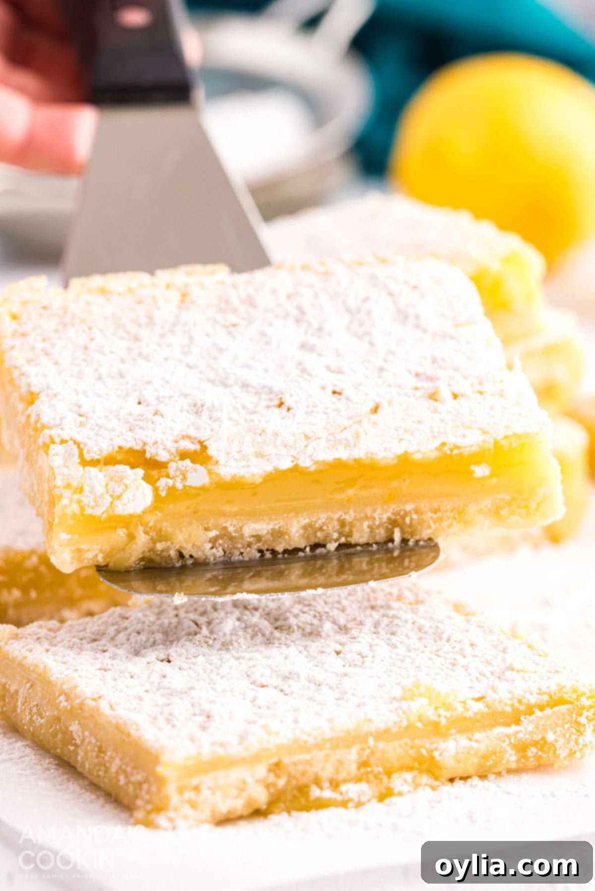 A single lemon bar being lifted from a plate with a spatula, powdered sugar dusted on top.
