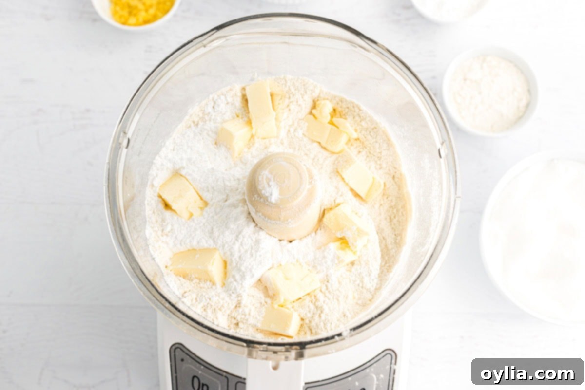 Food processor with flour, powdered sugar, and cubed butter, ready to be pulsed for the lemon bar crust.