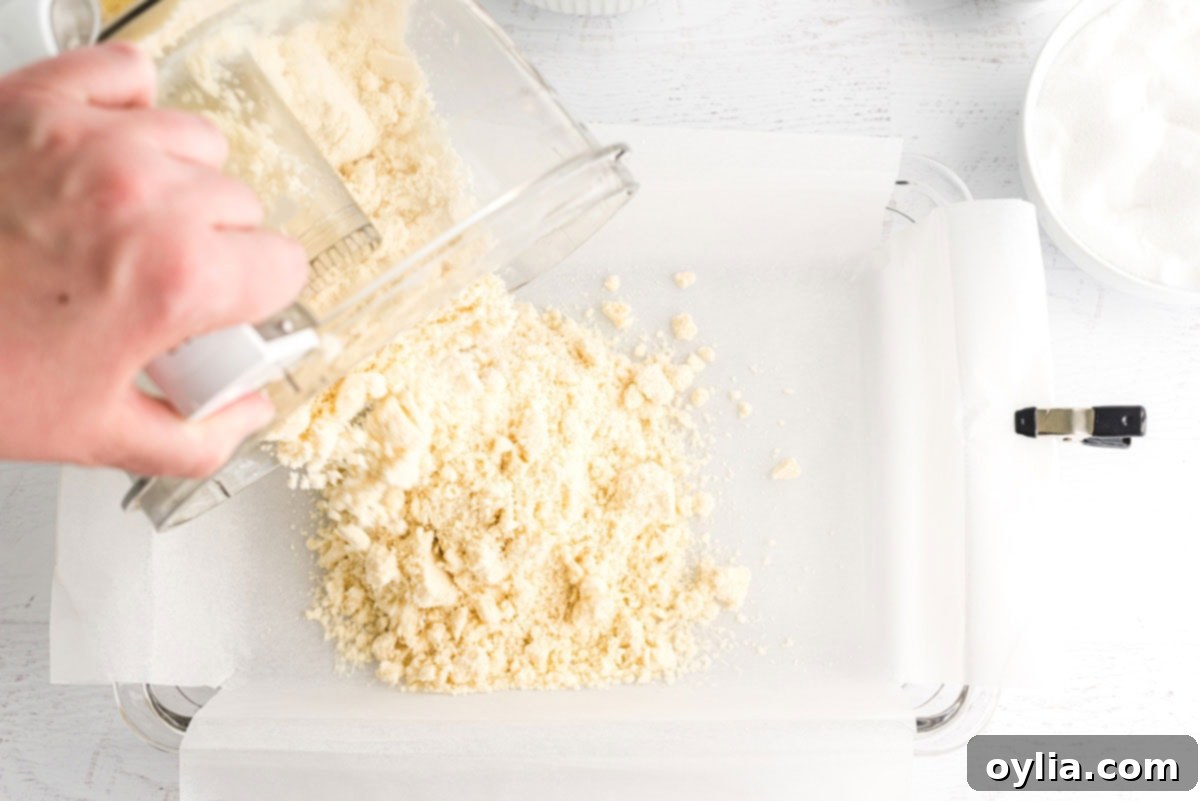 Pouring the shortbread crumb mixture into a parchment-lined baking pan.