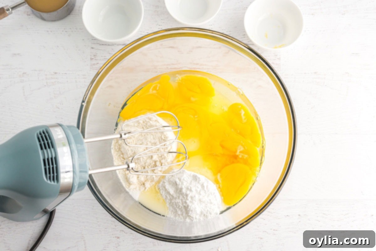 Eggs, sugar, flour, lemon juice, and zest being mixed in a bowl with an electric mixer for the lemon bar filling.