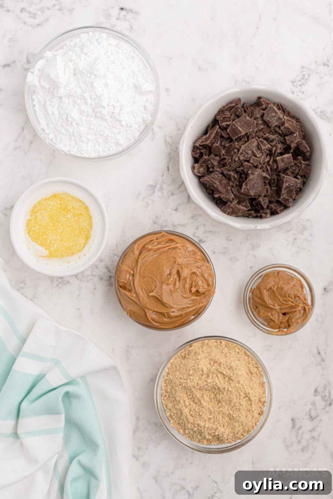 Collection of ingredients laid out for making no-bake peanut butter bars, including butter, crackers, powdered sugar, peanut butter, and chocolate.