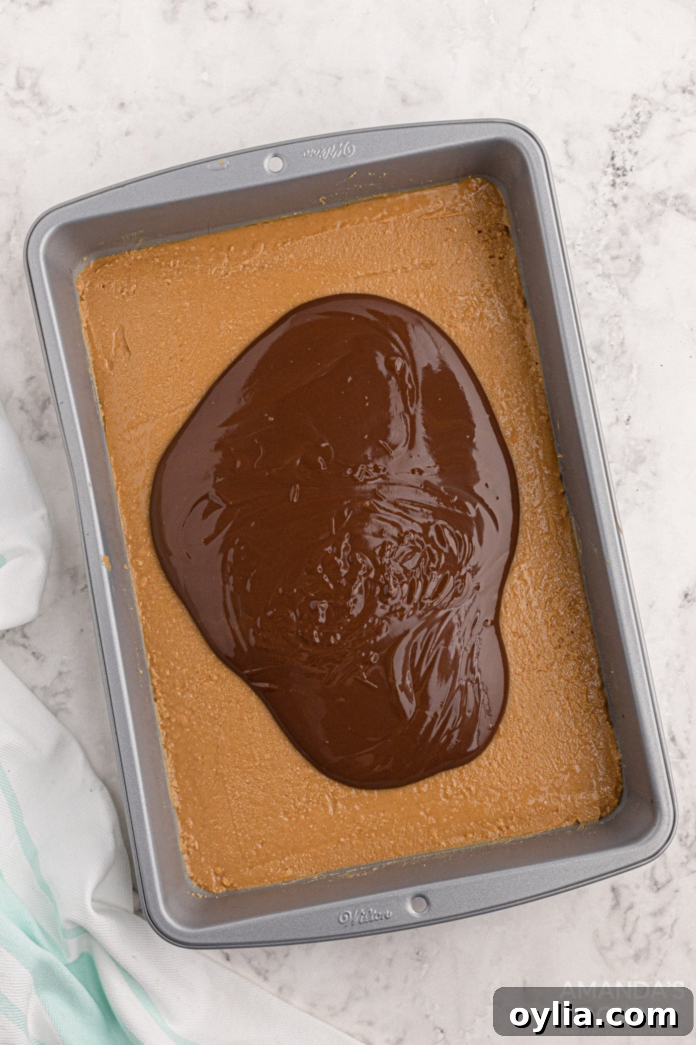 Melted chocolate and peanut butter topping spread over the peanut butter base in a baking pan, ready for chilling.