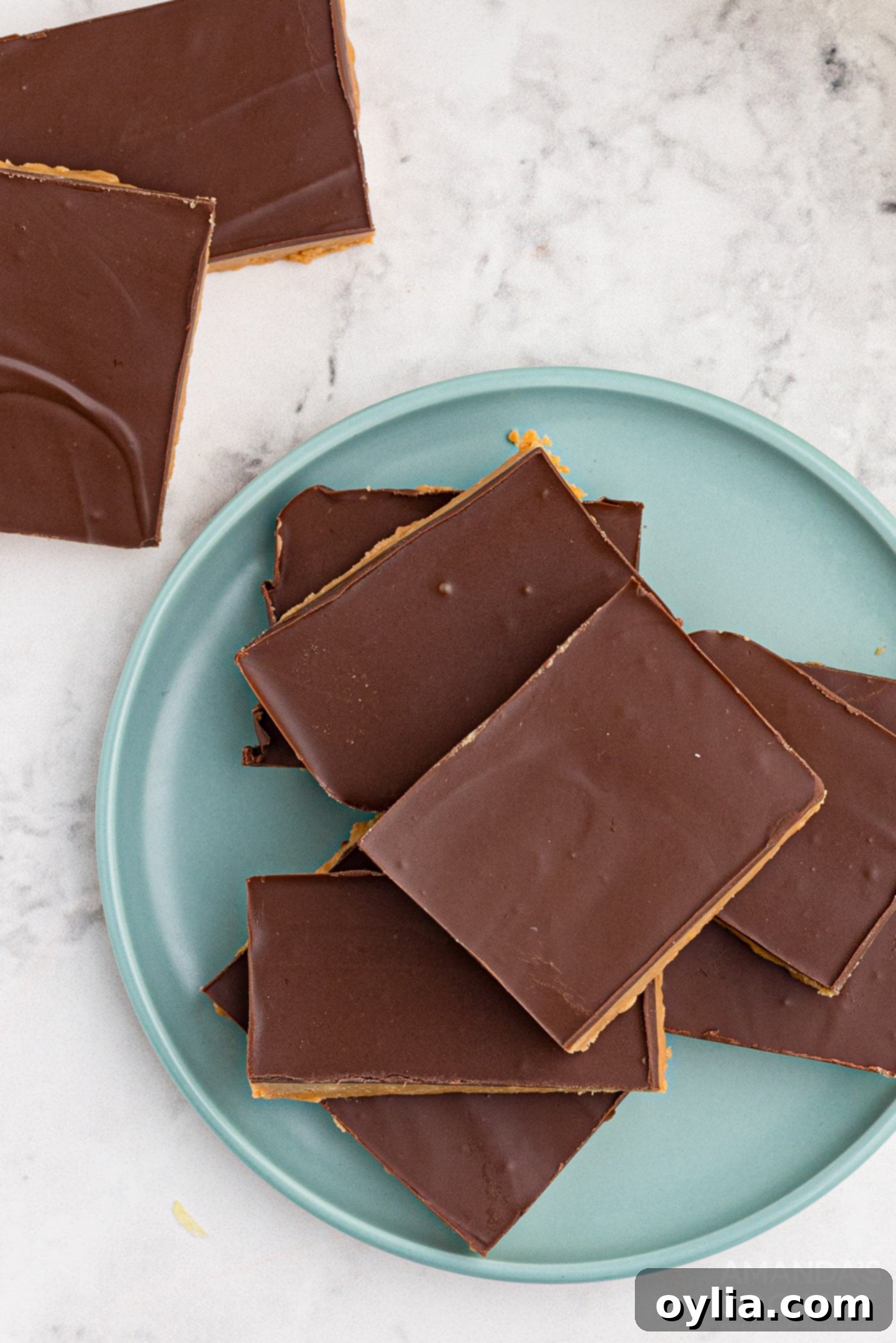 Three no-bake chocolate peanut butter bars with a smooth chocolate frosting, arranged on a white plate for serving.