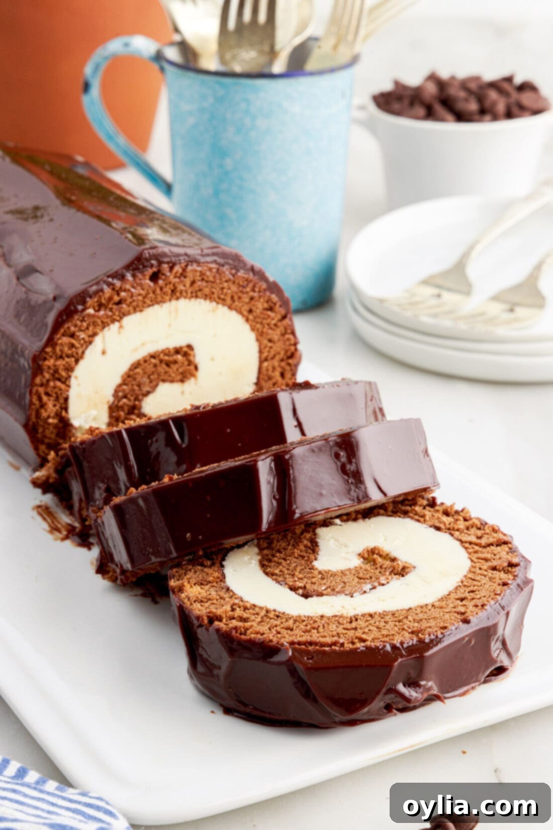 Decadent Chocolate Swirl 2 Swiss Roll cut in slices on a platter, showcasing the beautiful chocolate sponge and white buttercream swirl, topped with dark chocolate ganache.