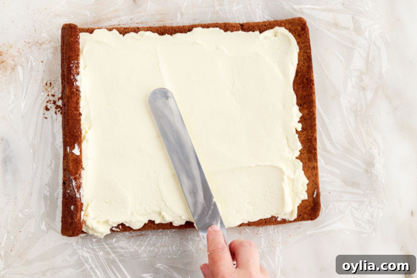 spreading frosting over a log cake evenly with an offset spatula