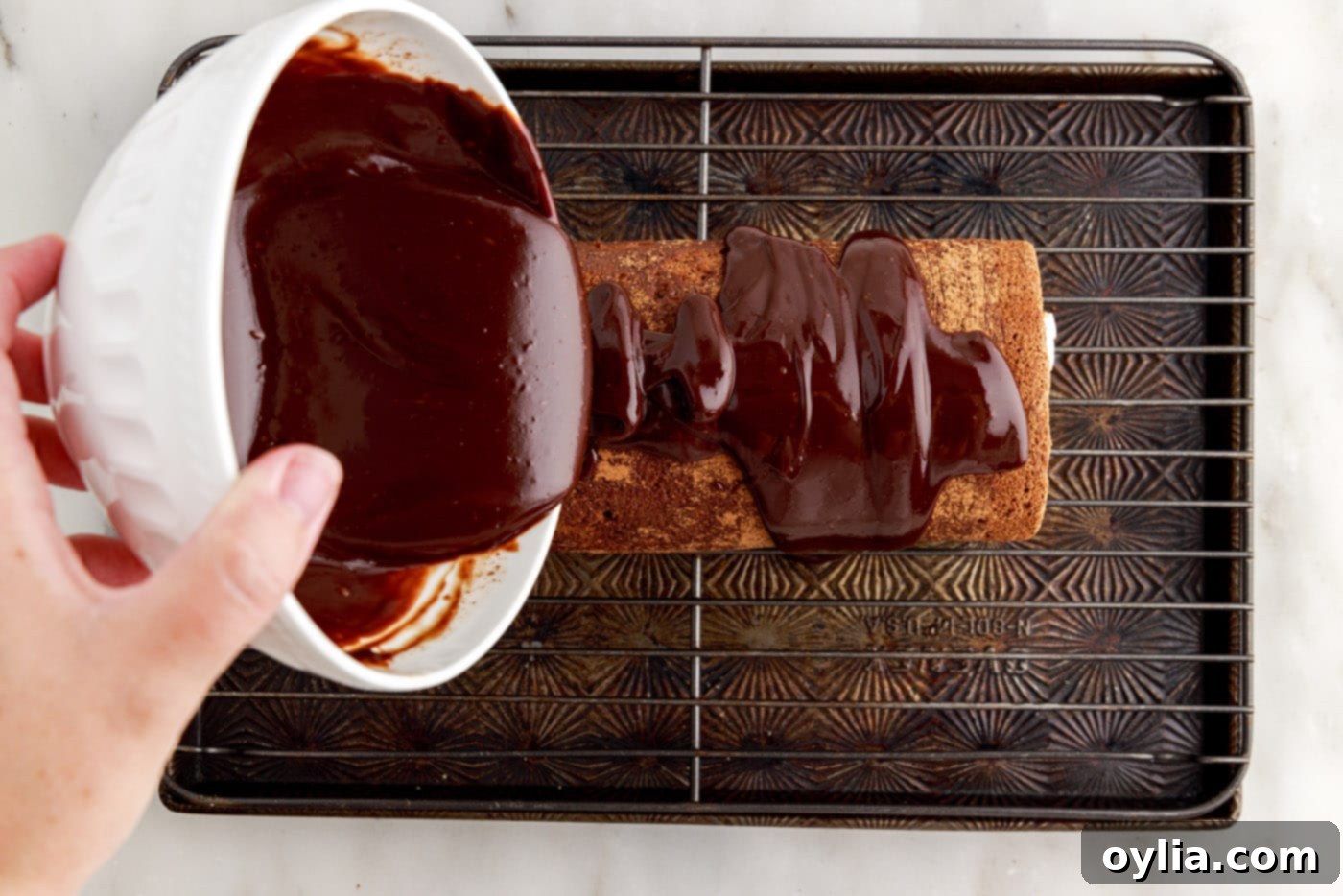 pouring chocolate ganache over a chilled swiss roll cake