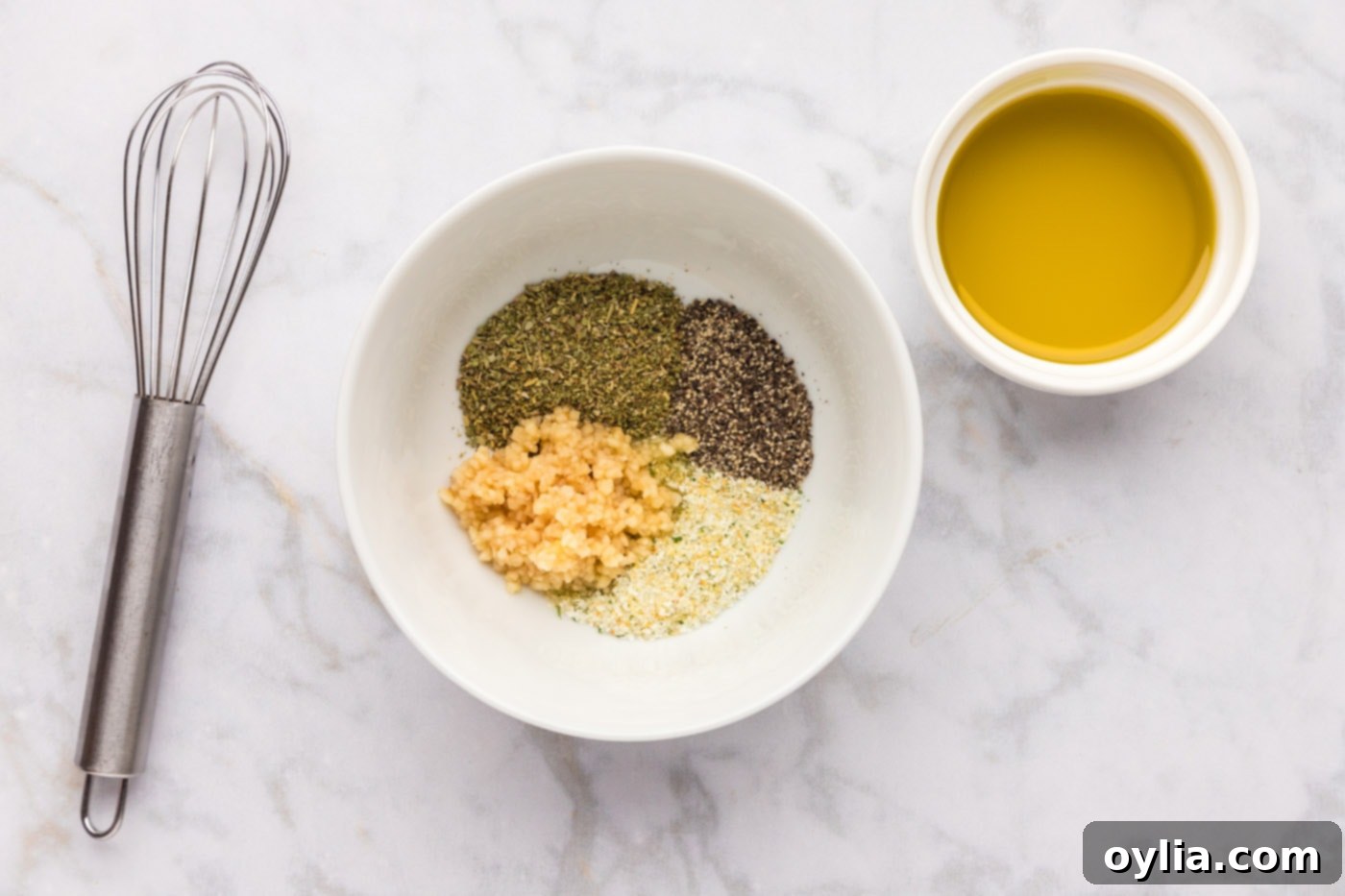 Close-up of minced garlic, garlic salt, black pepper, and Italian seasoning in a bowl before mixing.