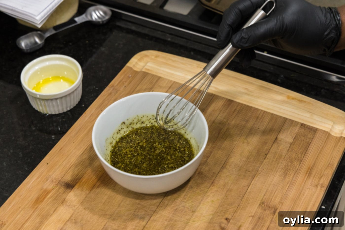 Hand whisking olive oil into a bowl of garlic and spice mixture for grilled zucchini.