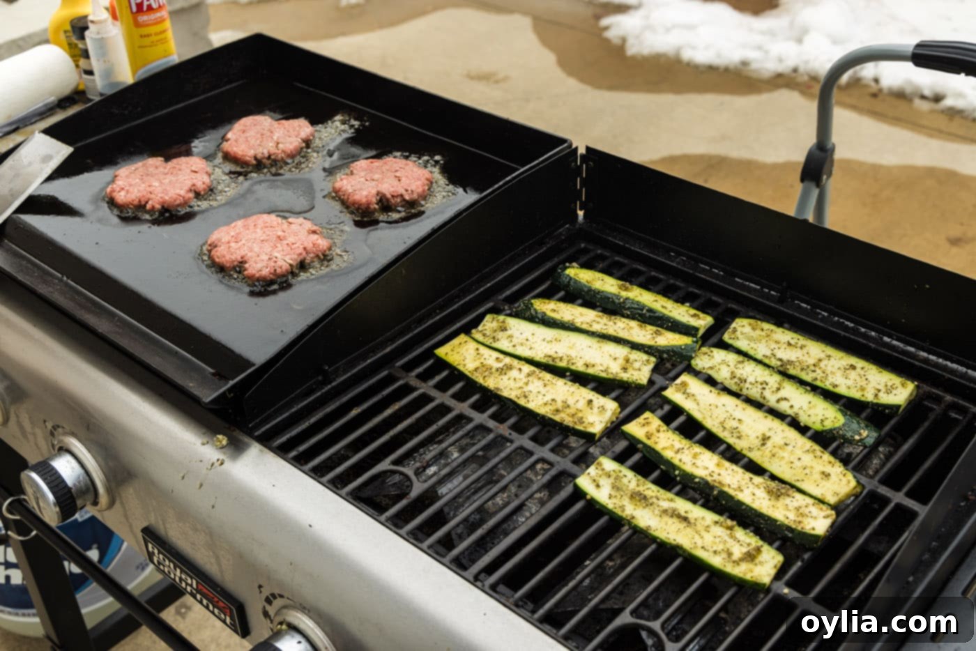 Grilled zucchini cooking on a flat top grill alongside burger patties for a complete meal.