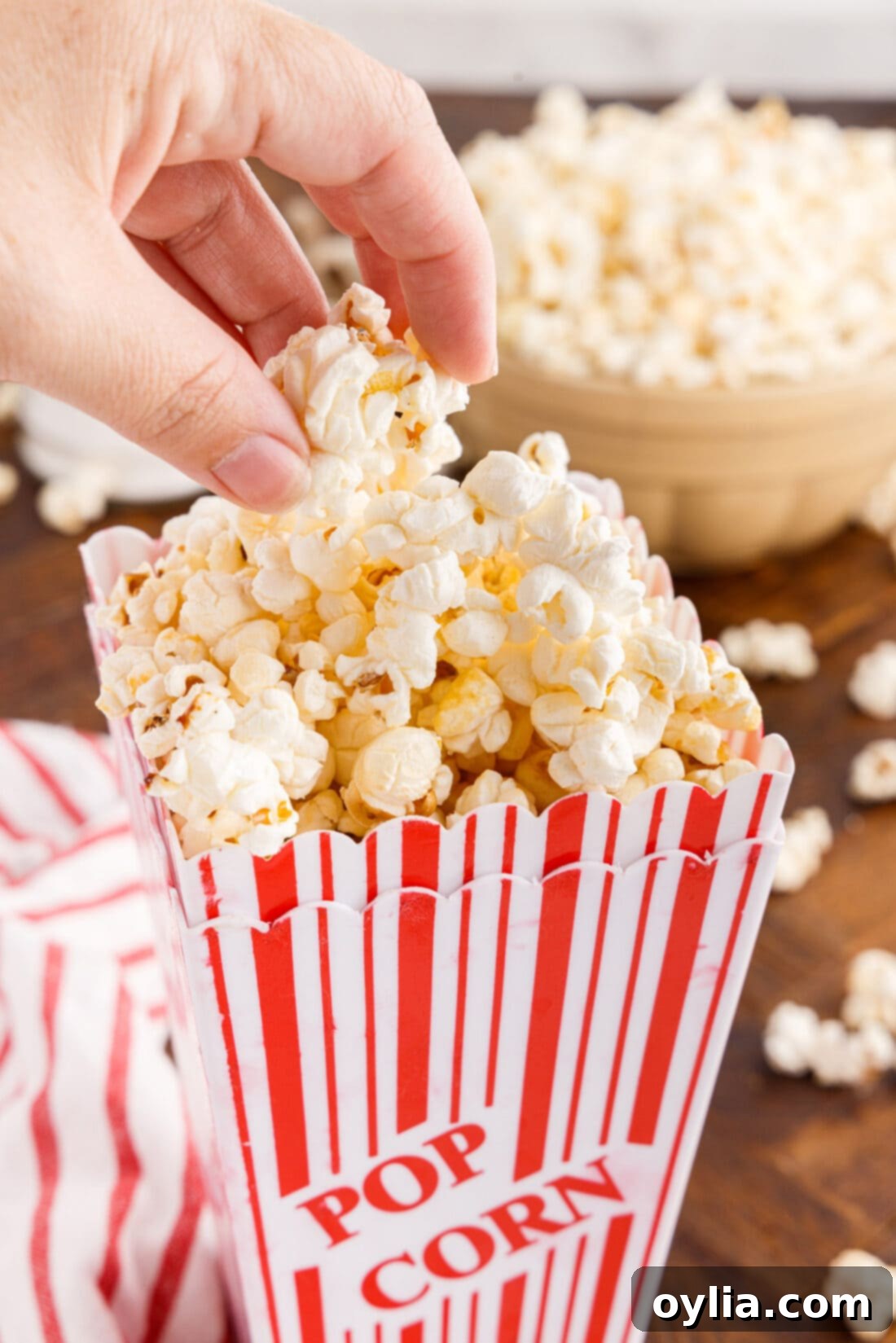 Hand reaching into a classic red and white striped popcorn bucket filled with fresh kettle corn.