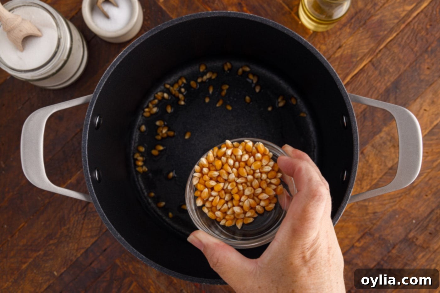 Adding corn kernels to shimmering oil in a pot, ensuring even coating.