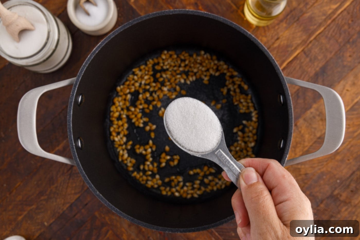 Sprinkling white granulated sugar over corn kernels in a hot pot.
