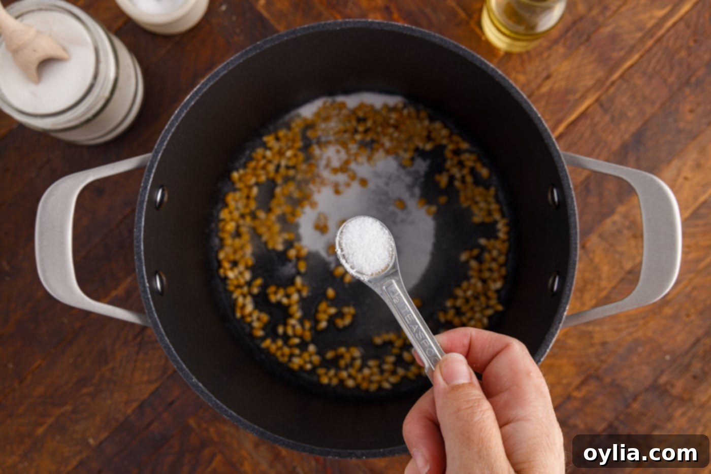 Adding fine sea salt to the sugar-coated corn kernels in the pot.