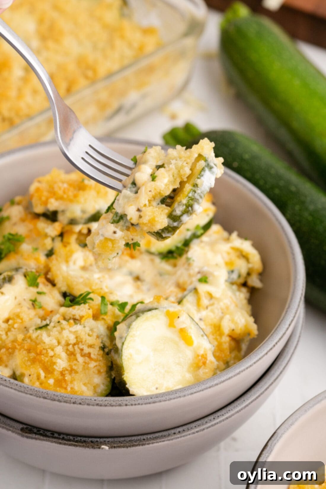 A fork lifting a piece of creamy, cheesy Zucchini Casserole from a bowl, showcasing its delicious texture and golden topping.