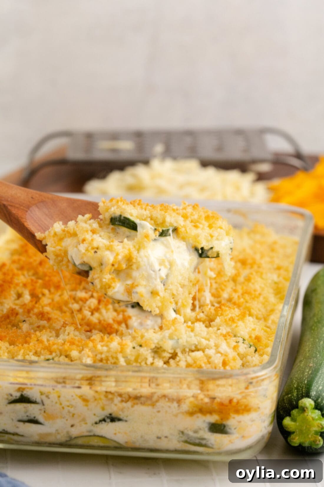 A serving of Zucchini Casserole on a spoon being lifted from a baking dish, showing the creamy texture and golden crust.