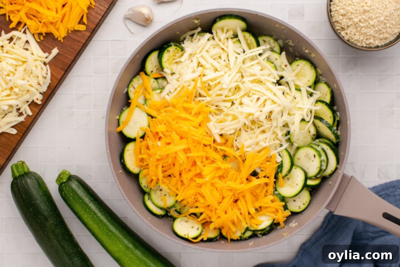Adding shredded cheddar and Monterey Jack cheese to the sautéed zucchini mixture in a skillet.