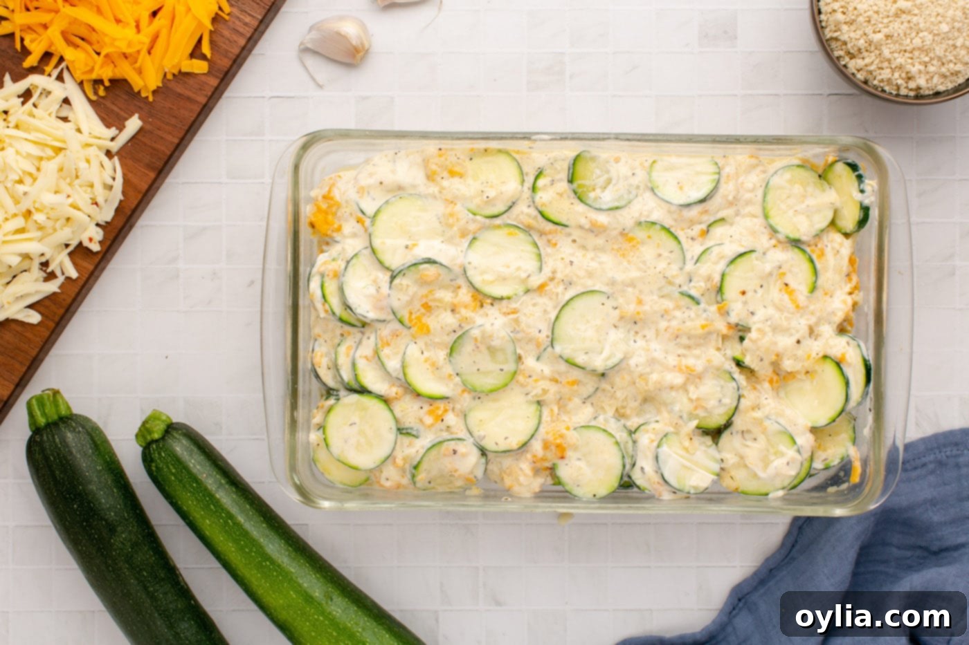 Spreading the cheesy zucchini and mayonnaise mixture evenly into a baking dish.