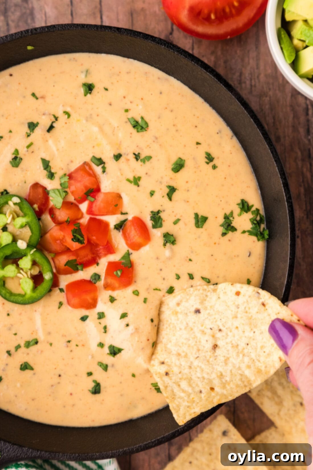 Tortilla chip being dipped into a skillet of Queso Dip
