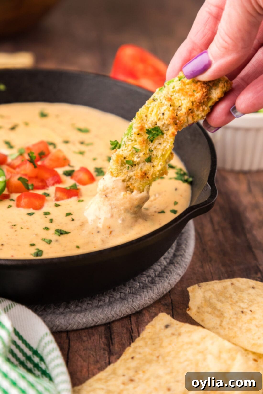 An air fryer avocado fry being dipped into a skillet of Queso Dip