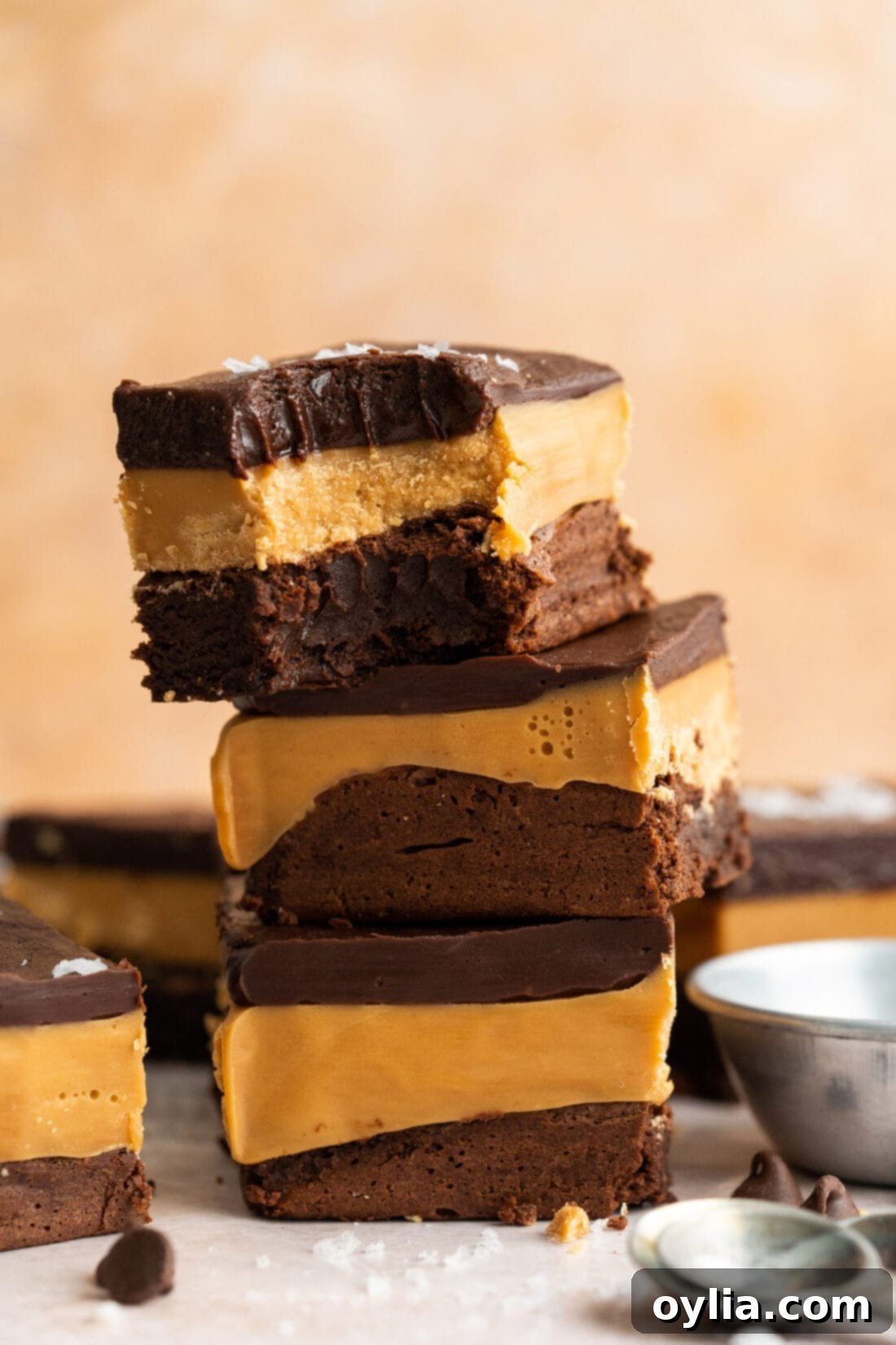 Ultimate Indulgence Brownies 2 Stack of three Millionaire Brownies with a bite removed from the top one, showcasing the distinct layers of brownie, caramel, and chocolate ganache
