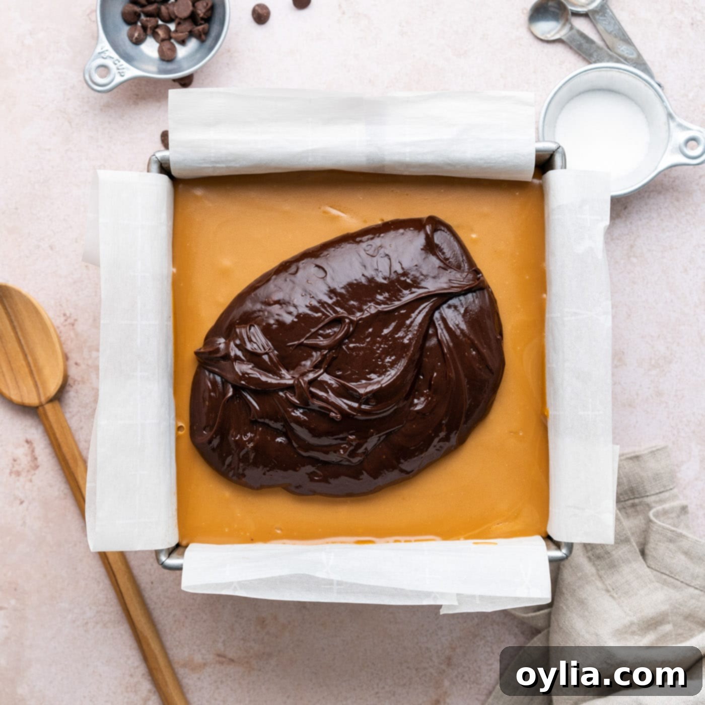 layering chocolate ganache over caramel on brownies in a pan