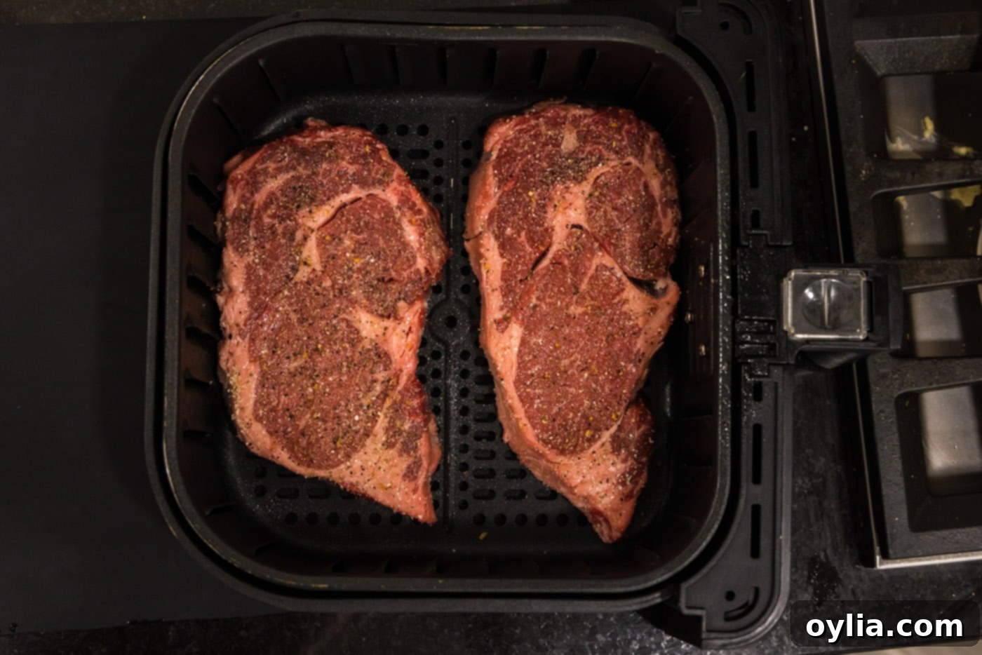 ribeye steaks cooking in the air fryer basket, beginning to brown