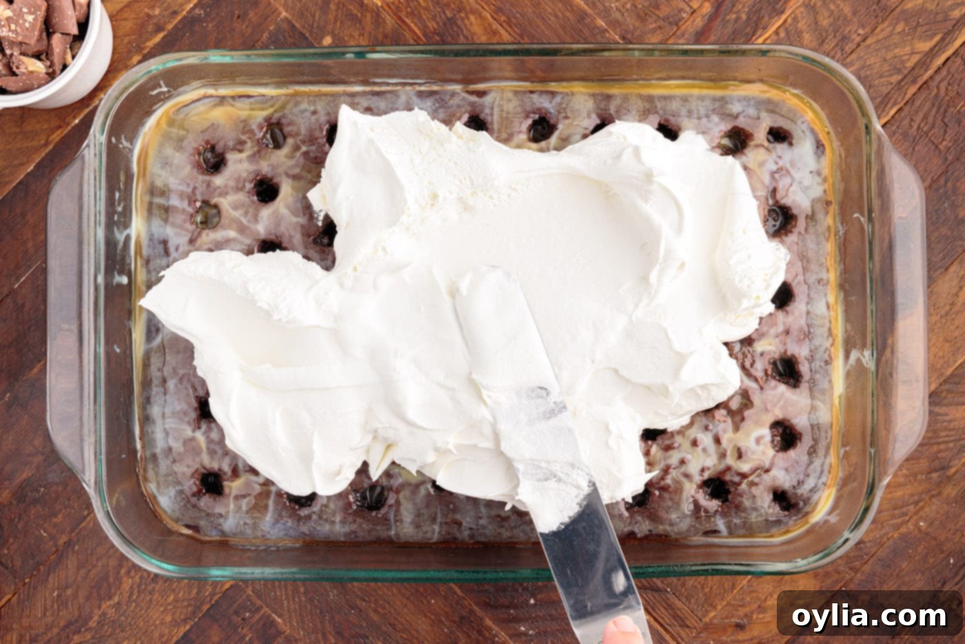 Spreading Cool Whip whipped topping smoothly over the chilled poke cake.