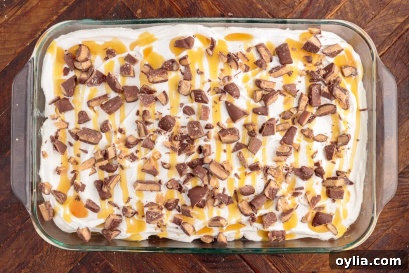 Final touches: drizzling caramel and sprinkling chopped toffee bits over the Cool Whip topped cake.