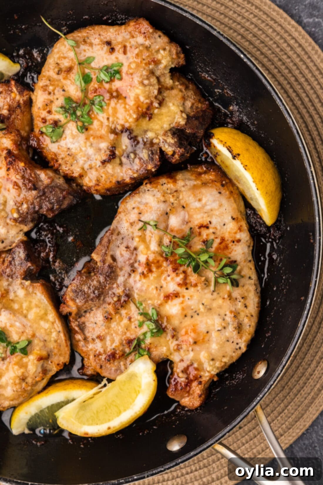 Close up photo of perfectly seared garlic butter pork chops in a skillet, smothered in sauce and fresh herbs