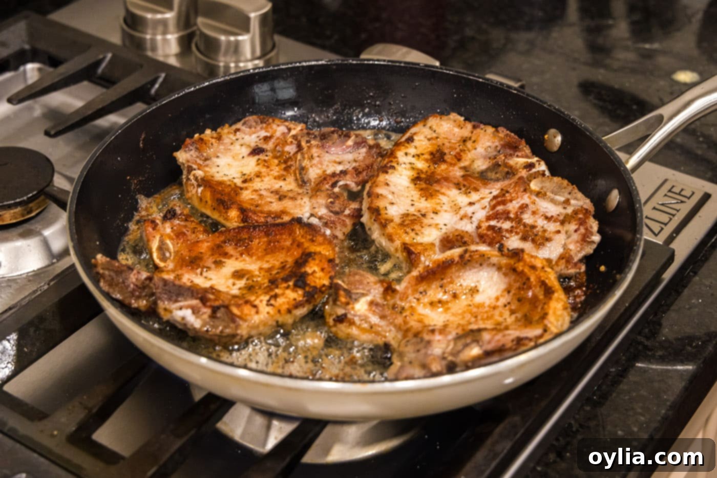 Pork chops flipped in the skillet, revealing a perfectly seared golden-brown crust on one side.