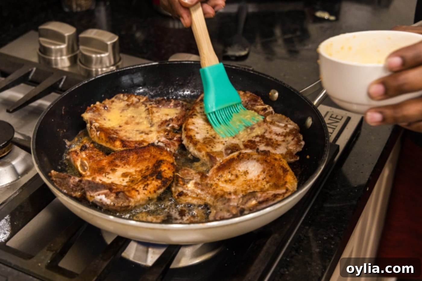 A basting brush applying generous amounts of savory garlic butter over cooking pork chops in a skillet, infusing flavor.
