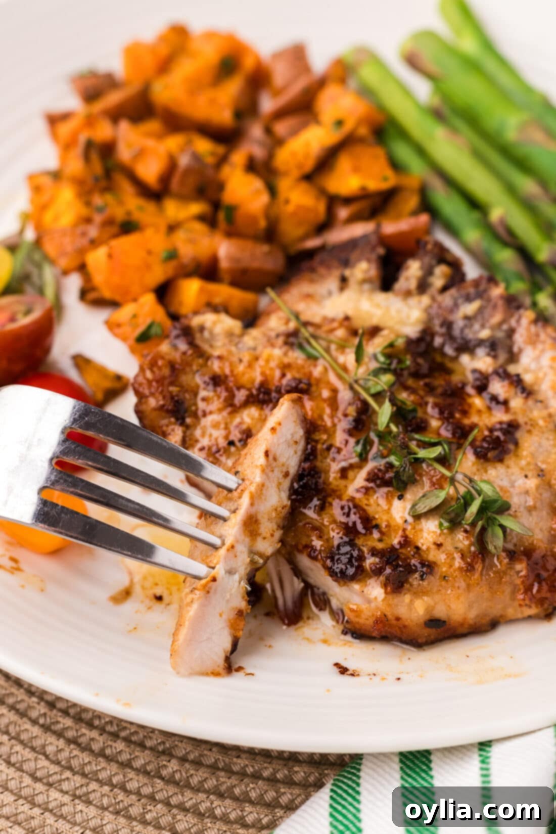 A fork holding a piece of juicy garlic butter pork chop, with another full chop and pan juices in the background.