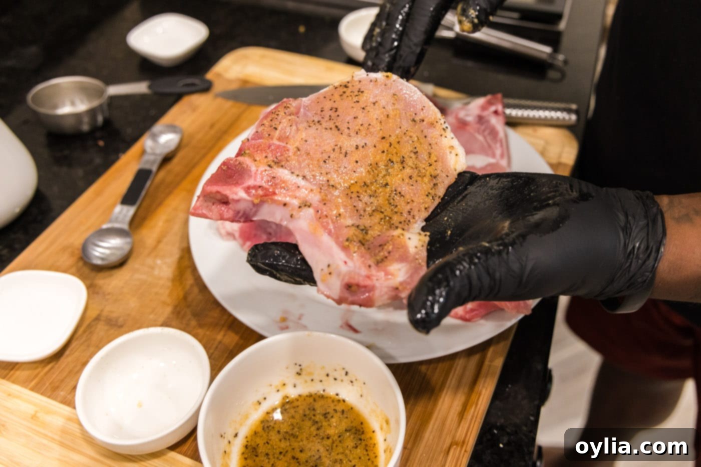 Hands applying the homemade seasoning rub evenly onto a raw pork chop, ensuring full coverage.