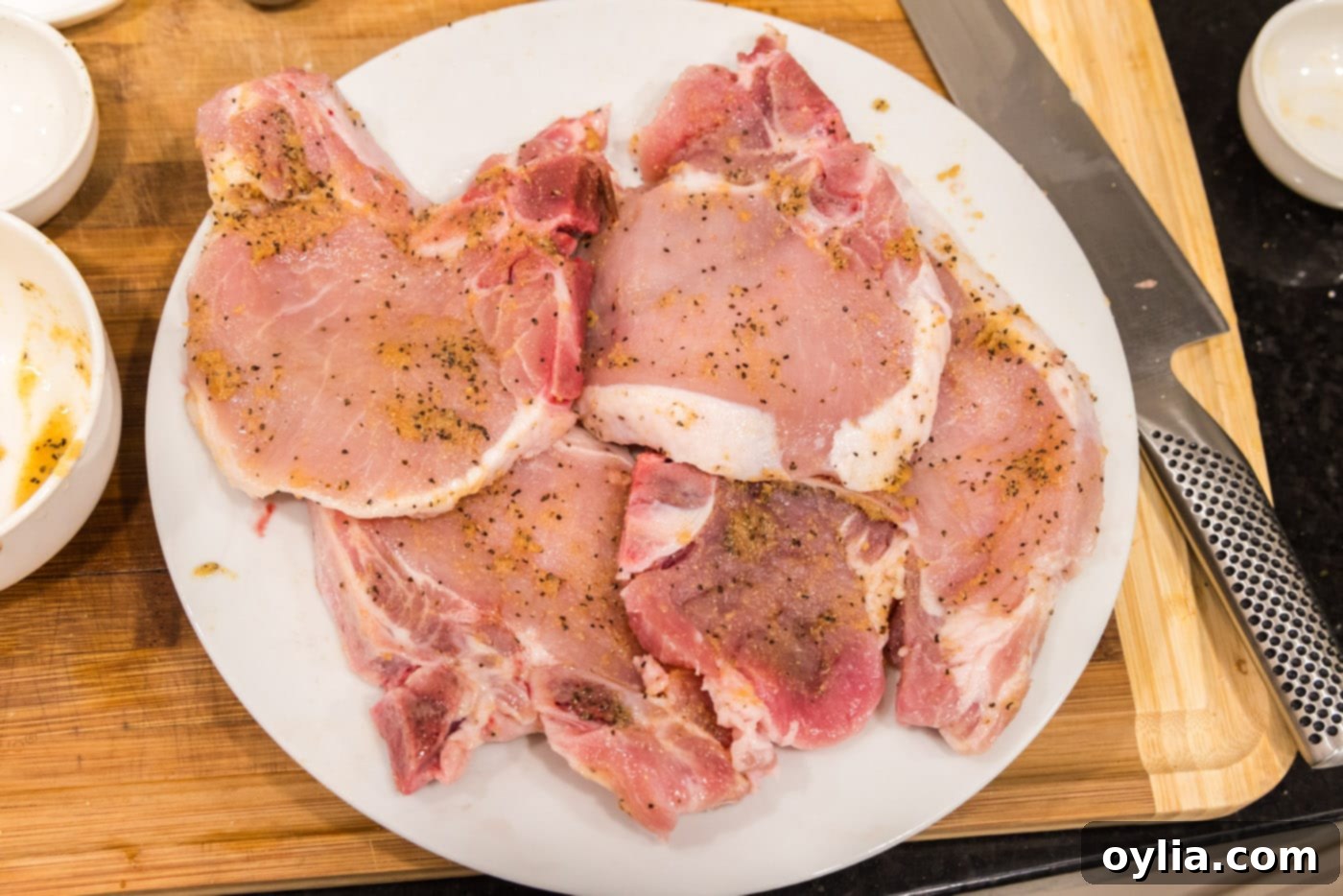 Two pork chops fully coated with the aromatic seasoning rub, perfectly prepared for searing.