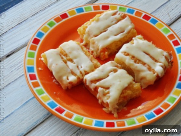 A close up photo of a single tropical dream dessert bar on an orange plate, showing its layers and delectable glaze.