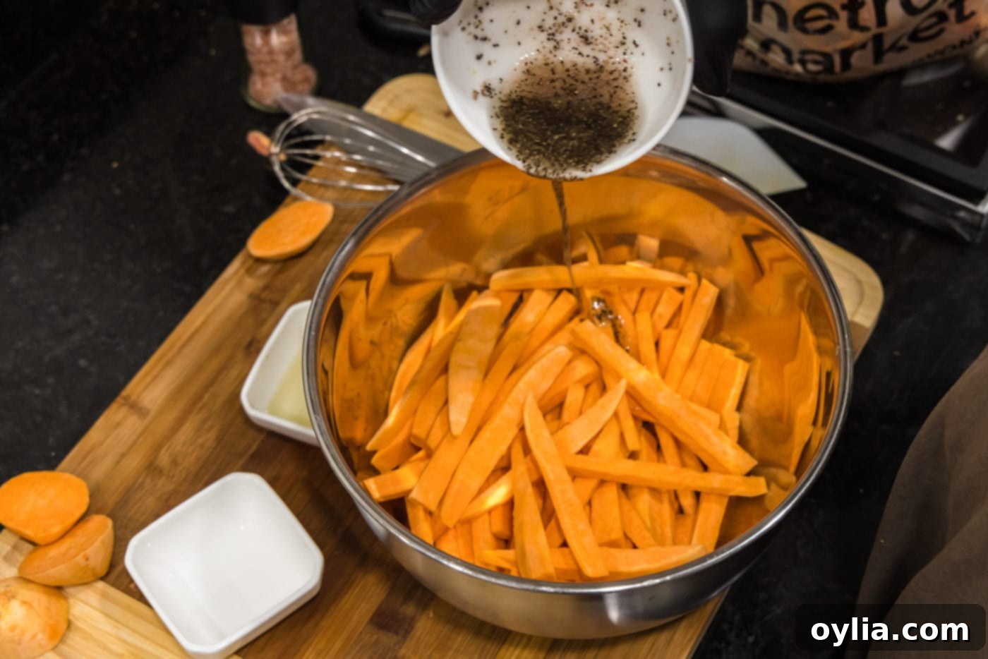 pouring olive oil and seasoning mixture over sweet potato fries in a bowl