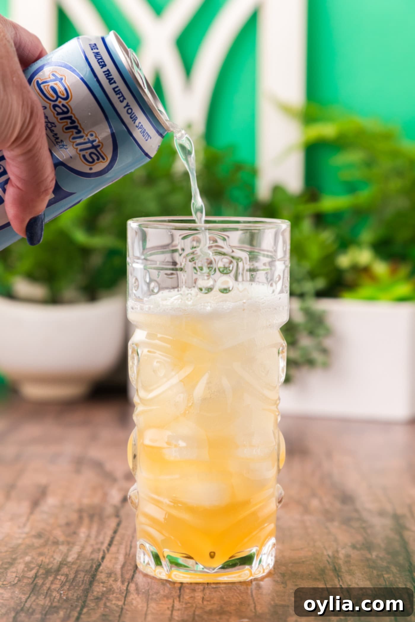 pouring ginger beer over rum and lime juice in a cocktail glass