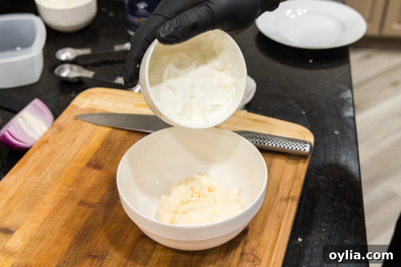 Whisking sour cream, mayonnaise, and white vinegar in a clear glass bowl for the salad dressing