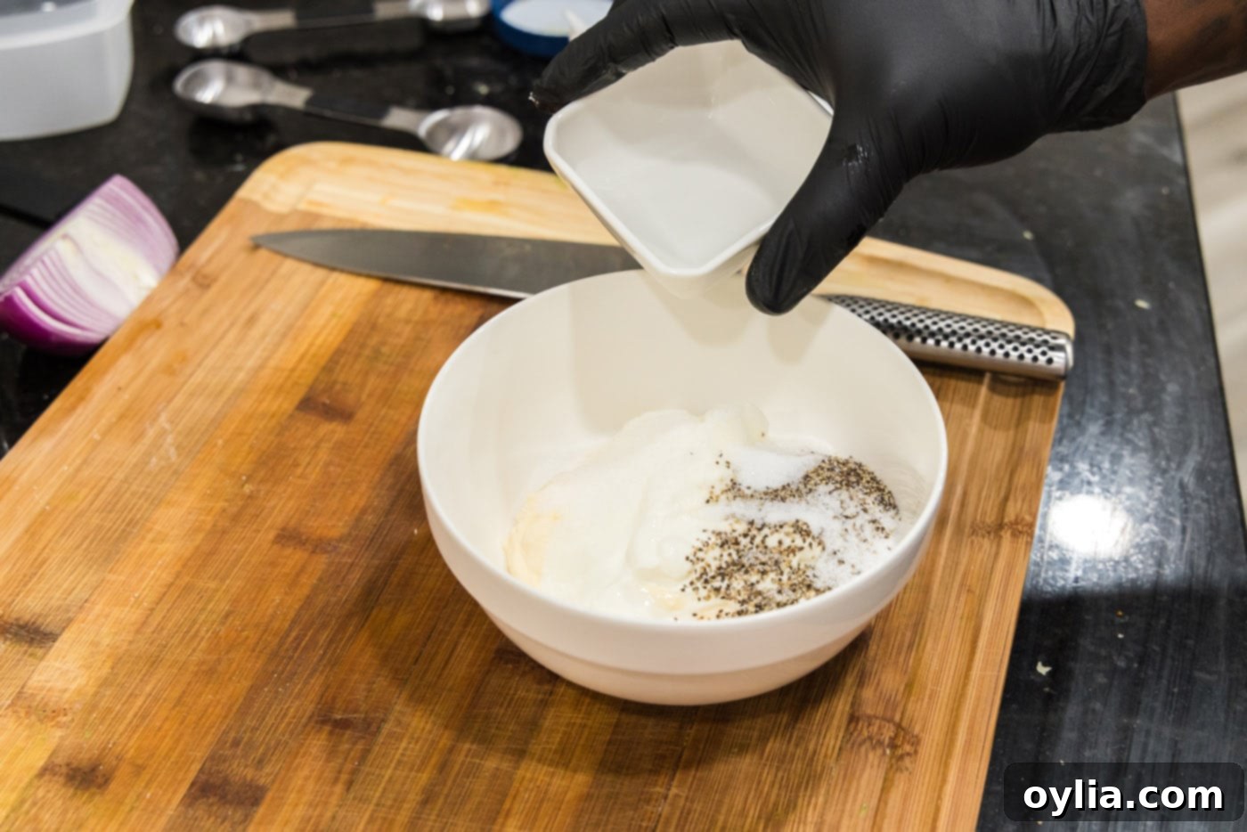 Adding a spoonful of sugar to the bowl containing mayonnaise, sour cream, and vinegar for the pea salad dressing