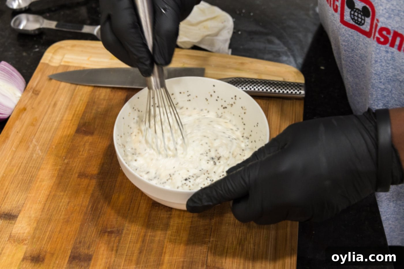 A whisk vigorously mixing the creamy pea salad dressing in a glass bowl until smooth