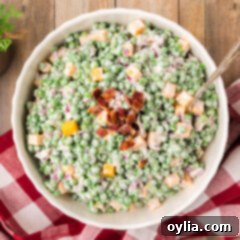 Overhead photo of a generous serving of Creamy Pea Salad topped with crispy chopped bacon in a white bowl, ready for serving