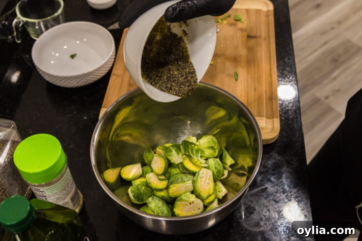pouring olive oil mixture over fresh brussels sprouts in a large mixing bowl