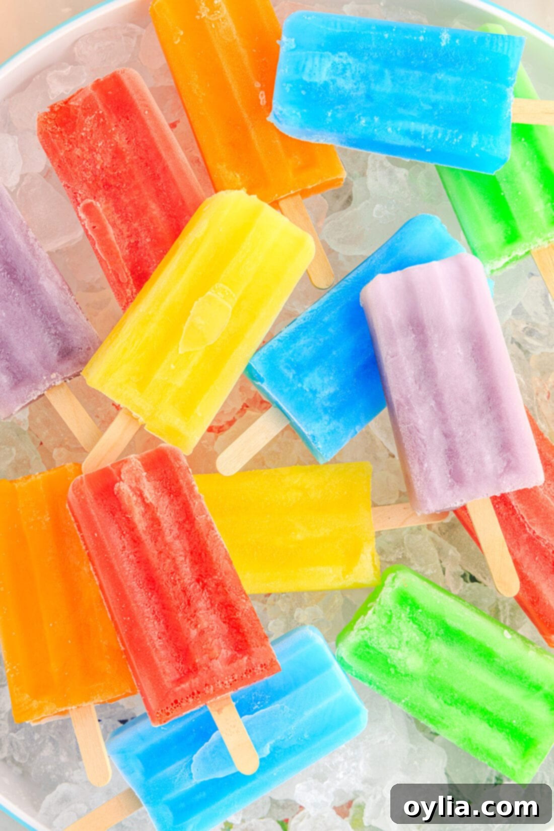Close up photo of an assortment of Jello Popsicles resting over a bowl of ice, showcasing a variety of vibrant colors like red, orange, yellow, green, and purple, highlighting their refreshing and appealing look.