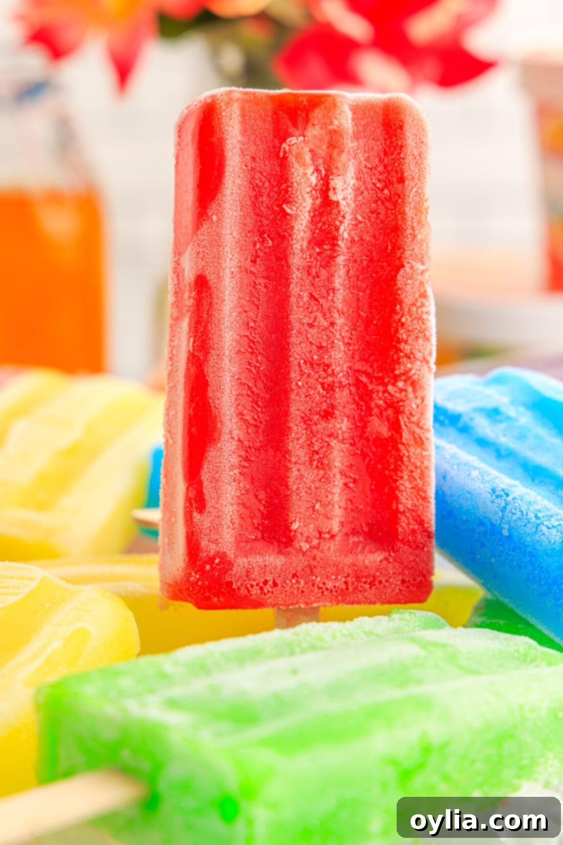 A single vibrant red Jello Popsicle standing prominently in a bowl filled with other assorted Jello Popsicles and ice, perfectly showcasing its texture and festive color.