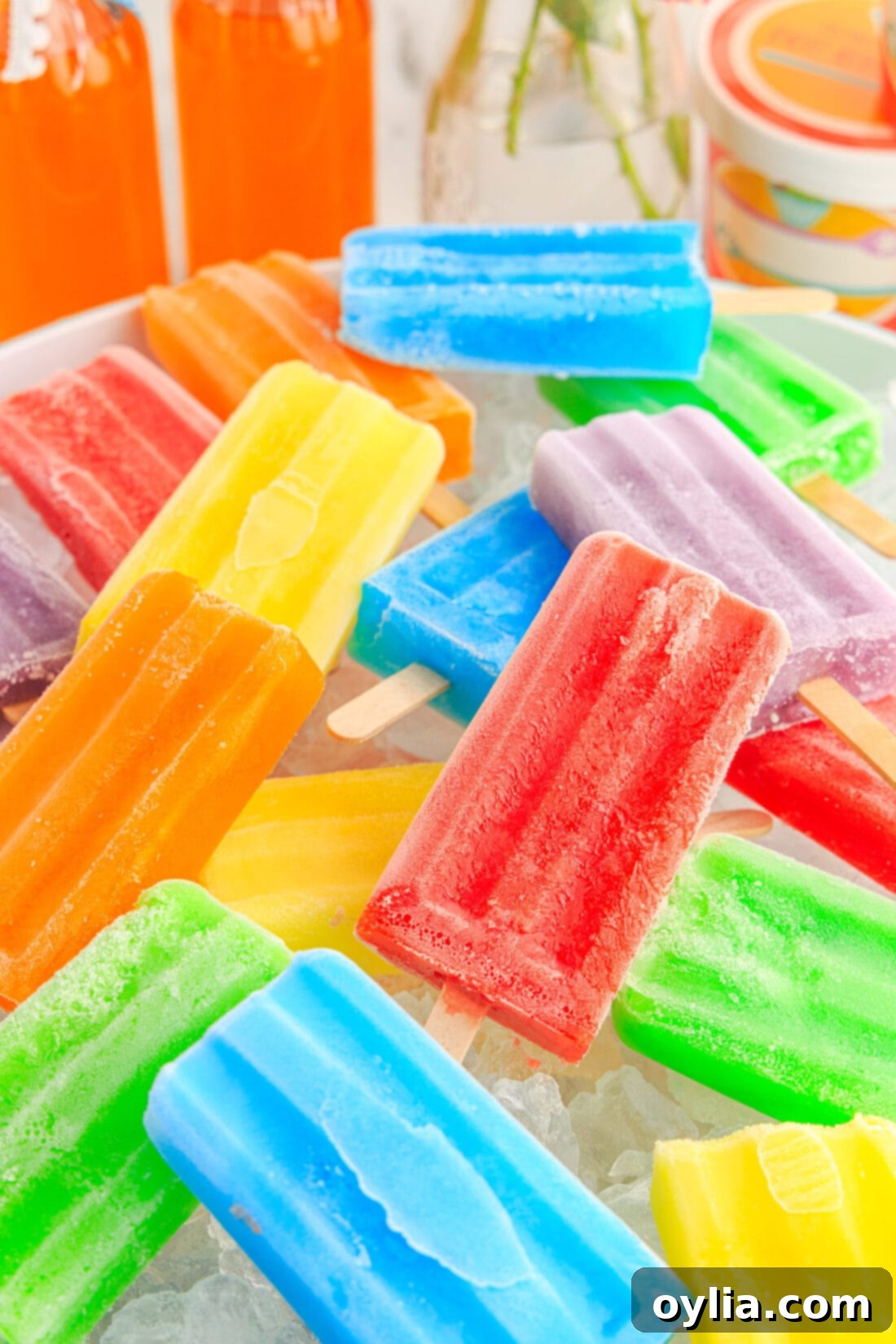 A colorful array of Jello Popsicles arranged in a clear bowl filled with ice cubes, emphasizing their coolness and variety.