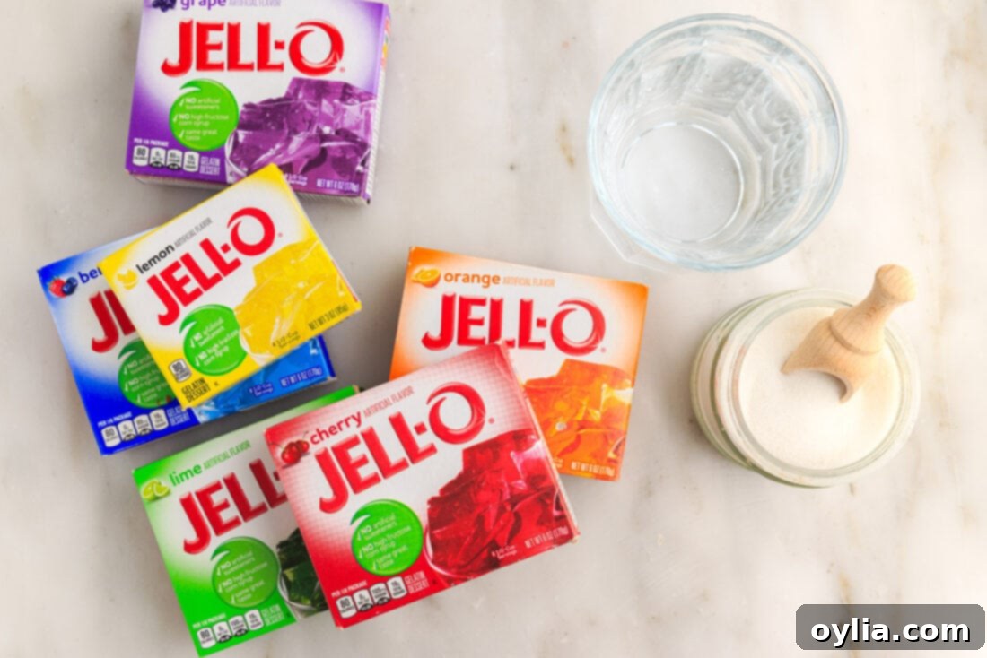 Close-up of the essential ingredients for Jello Popsicles: a vibrant packet of Jello powder, a bowl of granulated sugar, and a glass of water, neatly arranged on a kitchen counter.