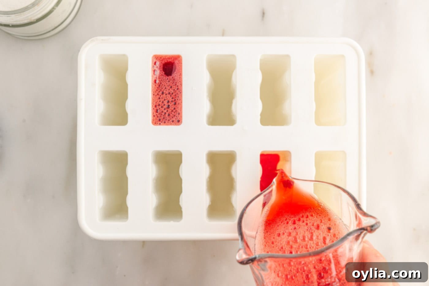 Red Jello mixture being poured into individual cavities of a popsicle mold, ensuring an even fill.