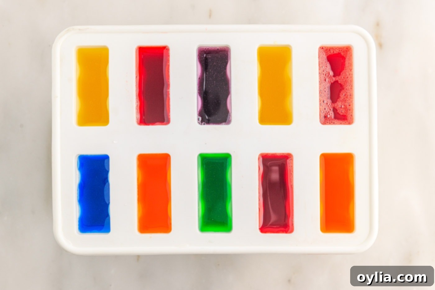 Close-up of a popsicle mold with multiple colorful Jello mixtures, showing the diversity of flavors.